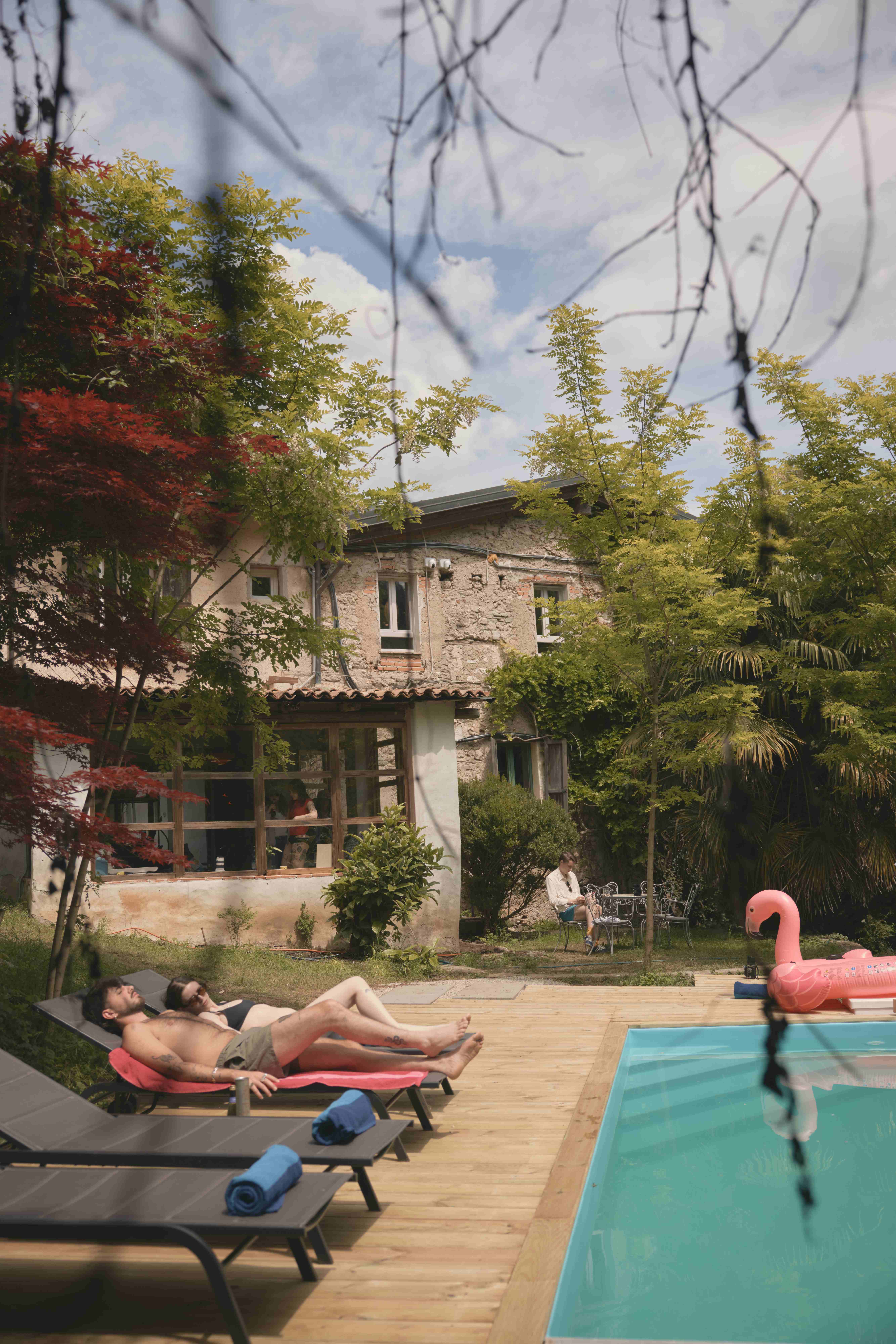 Guests relaxing on sun loungers beside the pool with the historic stone farmhouse behind
